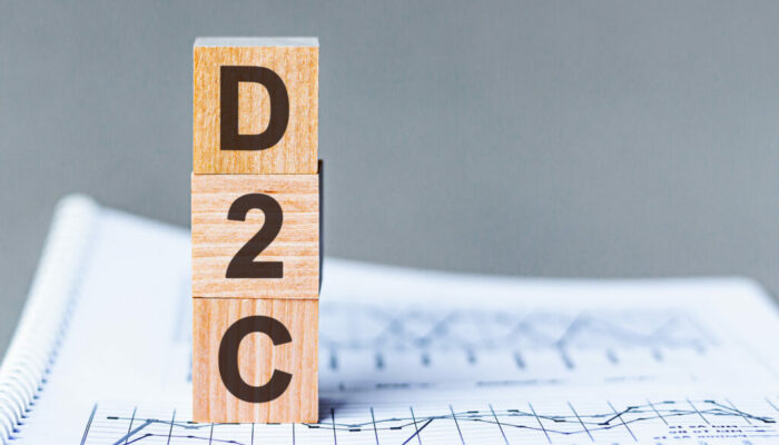 D2C - DTC Advertising Direct-to-Consumer - acronym on wooden cubes on columns of numbers background. D2C, acronym on wooden cubes. Background - document with numbers, business concept.