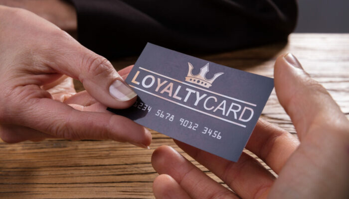 Human Hand Giving Loyalty Card To Another Person Over Wooden Desk