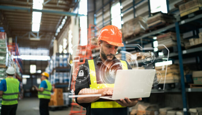 Professional manager man employee using laptop check stock working at warehouse. Worker wearing high visibility clothing and a hard hat, helmet and checking and count up goods or boxes for delivery.